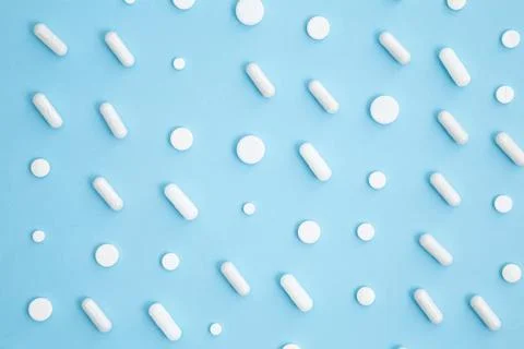 Various white medication tablets and capsules on blue background. Concept of  Stock Photos