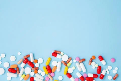 Various white medication tablets and capsules on blue background. Concept of  Stock Photos