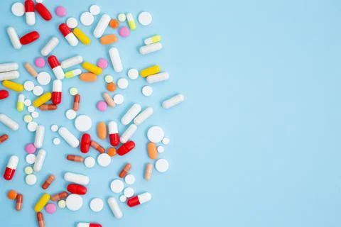 Various white medication tablets and capsules on blue background. Concept of  Stock Photos