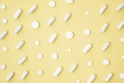 Various white medication tablets and capsules on yellow background. Concept o Foto stock