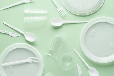 Various white plastic disposable tableware on green background. Stock Photos