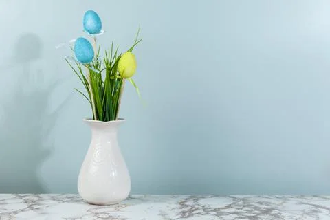 Vase with grass and Easter eggs, space for text, green background. Stock Photos