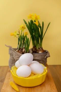 Vase with jonquil flowers, Easter eggs in basket and decor on shelf near wall Stock Photos