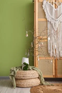 Vase with tree branches and Easter eggs on poufs in room Stock Photos