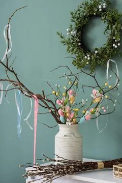 Vase with tree branches and Easter wreath on green wall in room Stock Photos