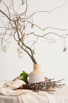 Vase with tree branches and Easter eggs on dining table near light wall Stock Photos