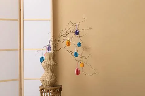 Vase with tree branches and Easter eggs on table near folding screen in room Stock Photos