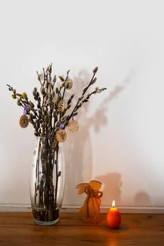 Vase with tree branches, candle and wooden toy rabbit on table near light wall. Stock Photos
