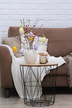 Vase with tree branches, Easter eggs and burning candle on table near the sofa Foto stock