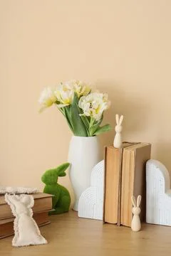 Vase with tulips, Easter rabbits and books on table near beige wall Stock Photos
