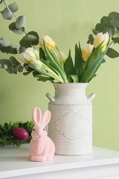 Vase with tulips, eucalyptus and Easter rabbit on shelf near green wall Stock Photos