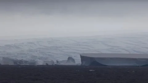Vast Antarctic glacier wall rises above dark polar water in a moody wide Vídeo Stock 335372216