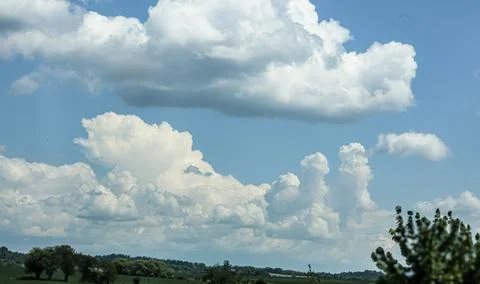 Vast blue sky filled with dramatic cumulus clouds over a green landscape 写真素材
