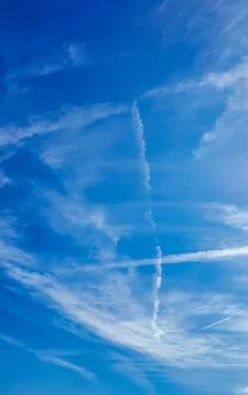 Vast Blue Sky With Wispy Clouds and Airplane Contrails Crossing Stock Photos