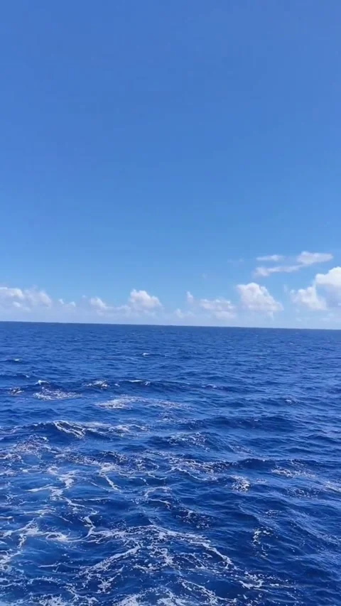 A vast, deep blue ocean under a clear sky with scattered white clouds on a sunny Vídeos de archivo 334163196