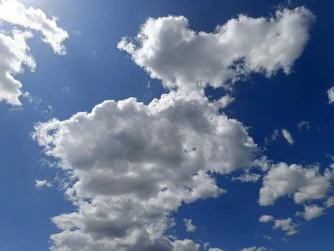 Vast, deep blue sky with textured white and grey cumulus clouds. Bright sun.. Stock Photos