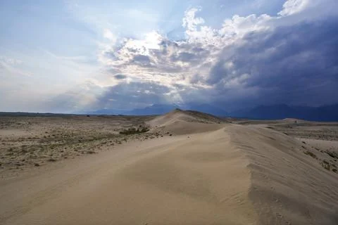 Vast desert dunes under a dramatic sky with sunbeams Stock Photos
