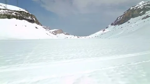 Vast frozen lake surface surrounded by high snow peaks in alpine valley with Stock Footage 344240755