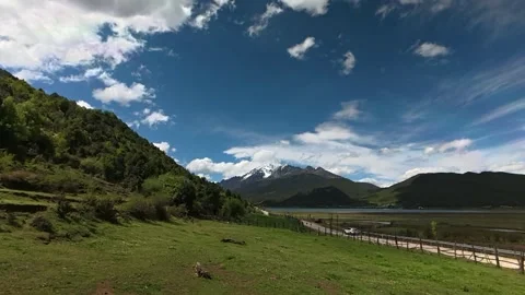 Vast Green Fields Slope Towards a Plateau Lake with Snow-capped Mountains in 库存影片 338211360