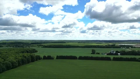 A vast landscape with green fields, a patch of forest, and a cloudy sky Stockbeeldmateriaal 304985172