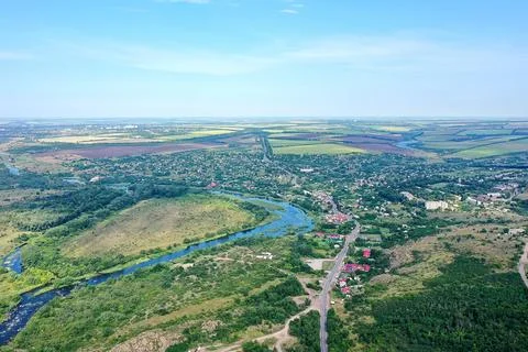 A vast landscape shows green fields, a winding river, and small houses spread Stock Photos