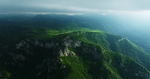 Vast Mountain Range Cliffs Ledges Overlooking Small Village Aerial Orbit Shot Stock Footage 300480051