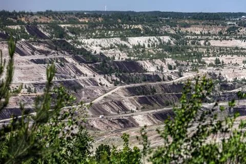 Vast open-pit mine with layered terraces and scattered green trees under a .. Stock Photos