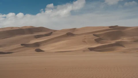 Vast Rolling Sand Dunes Beneath Blue Sky and Soft Cloud Formations Stock Footage 343025396