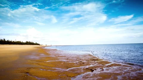 A vast sandy beach meets the blue ocean under a partly cloudy sky Stock Footage 312304361