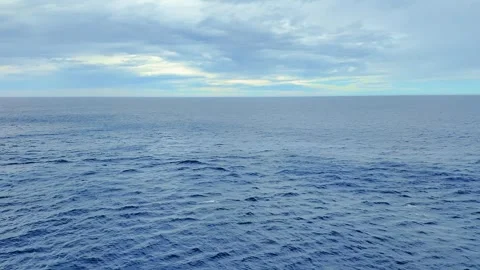 Vast, tranquil ocean with gentle waves under a cloudy, pale blue sky Stock Footage 324399386