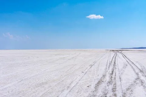 Vast white salt flat under a clear blue sky with scattered clouds Фото