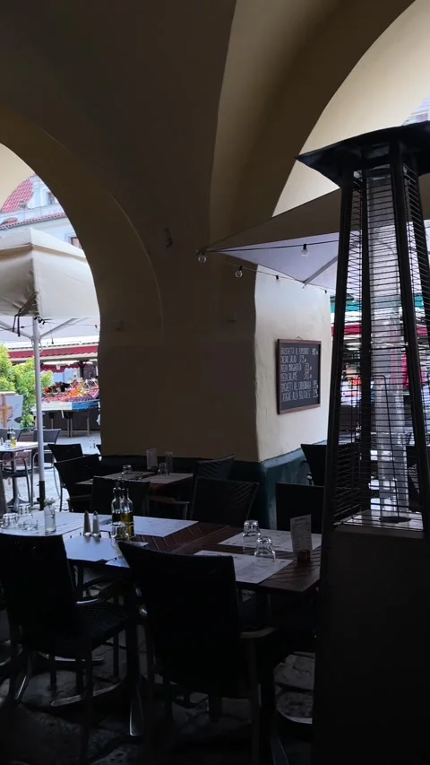 Vaulted arcade cafe with patio heater framing bright market street through arch 库存影片 344584916