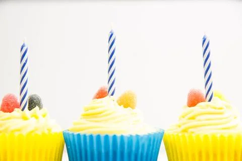 Vector art showing three yellow-frosted cupcakes blue striped candles, gumdrops Stock Photos