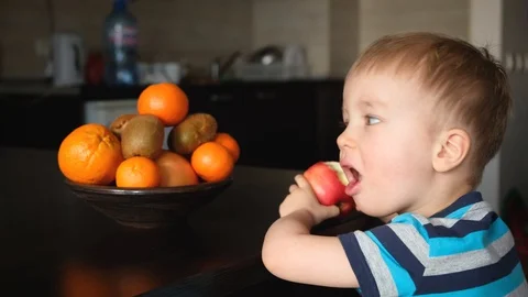 Vegan child eats and chews apple, vegetarian kid in kitchen, healthy food Видео 126998198
