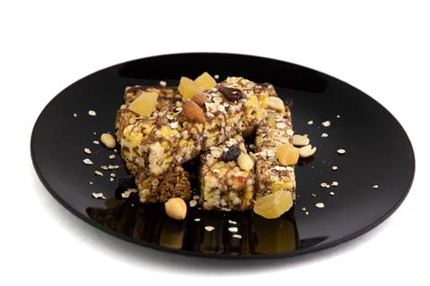 Vegan diet: several cereal bars with nuts, raisins and honey, in a black plat Stock Photos