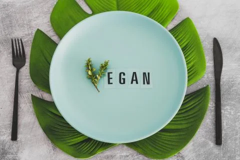 Vegan text with V made from small branches with leaves on plate with tropical Stock Photos