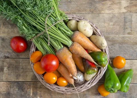 Vegetable basket on a wooden table, in rustic style. Stock Photos