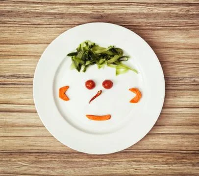 Vegetable face made of cucumber, chilli, tomatoes and carrot on the white pla Stock Photos