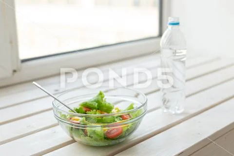 Vegetable salad and bottle of water lie on a white windowsill. Concept of Stock Photos