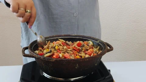 Vegetables and meat are stewed in a deep cast-iron skillet, with a female h.. 库存影片 343984714