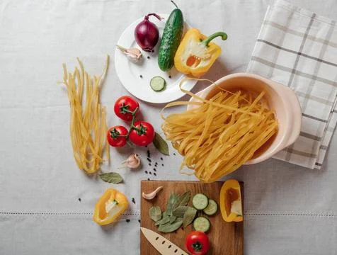 Vegetables and raw pasta on a table. Cherry tomatoes, yellow bell pepper, c.. Stock Photos
