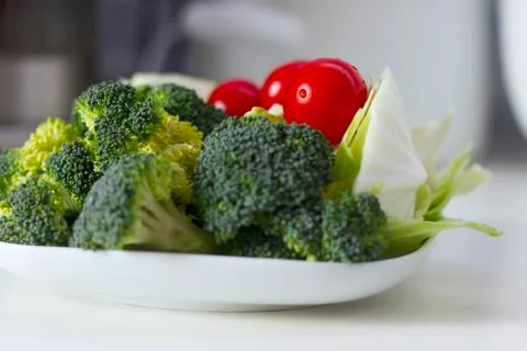 Vegetables (cabbage, tomato, broccoli) on a white plate on a white table Stock Photos