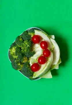 Vegetables cabbage, tomato, broccoli on a white plate on a green backround. Stock Photos