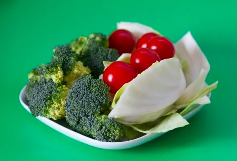 Vegetables cabbage, tomato, broccoli on a white plate on a green backround. Stock Photos