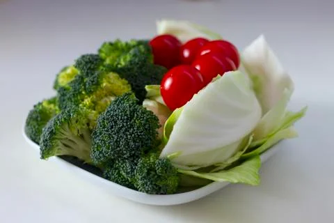 Vegetables (cabbage, tomato, broccoli) on a white plate on a white table Stock Photos