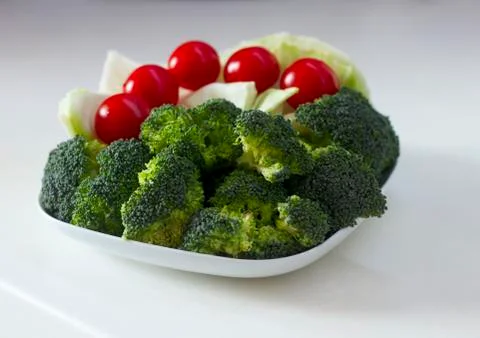 Vegetables (cabbage, tomato, broccoli) on a white plate on a white table Stock Photos
