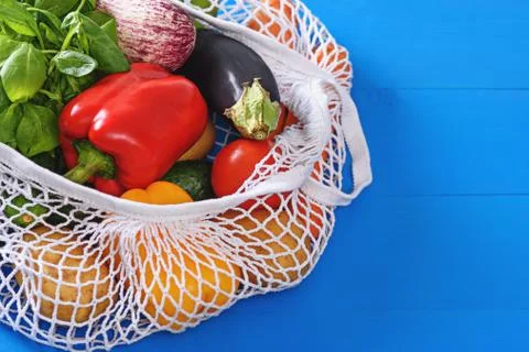 Vegetables in white string bag, crops on blue background, natural organic foo Stock Photos