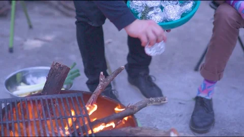 Vegetables wrapped in foil being put into the fire for baking Stock Footage 76101807