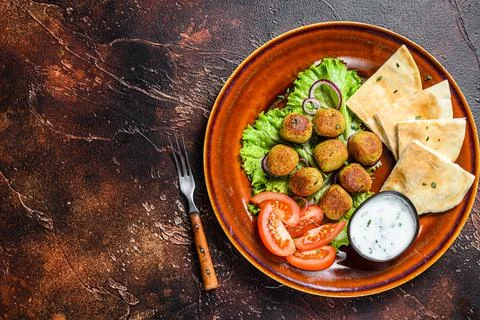 Vegetarian falafel with pita bread, fresh vegetables and sauce on a plate. Dark Stock Photos