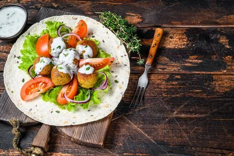 Vegetarian falafel with vegetables and tzatziki sauce on a tortilla bread. Dark Stock Photos